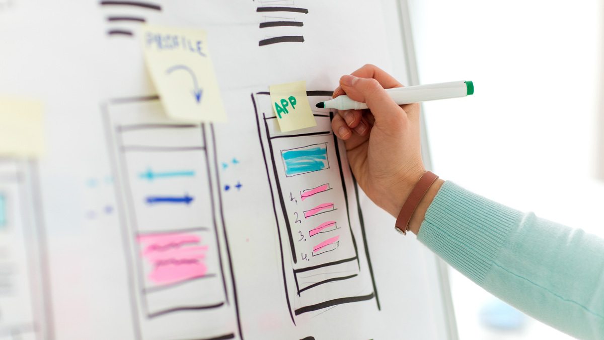 Close-up on UX designer's hands, writing on a stick note over a whiteboard mockup