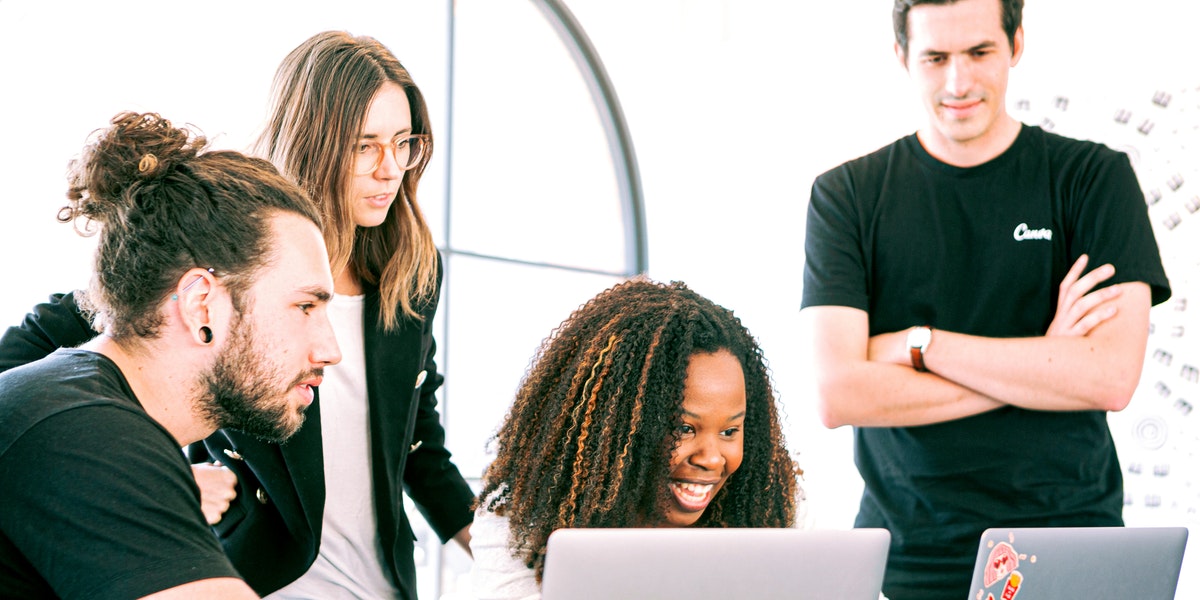 A group of developers in a meeting room looking at a pair of laptops discussing code