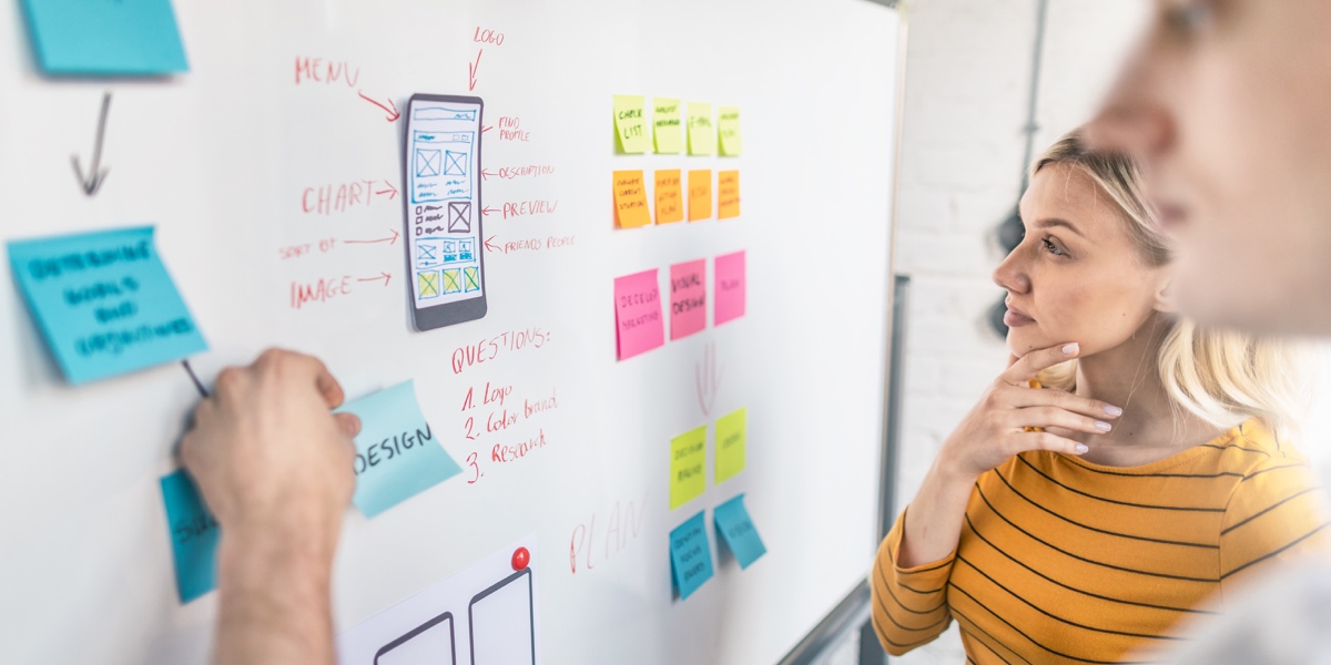 Two UX designers ideating at a whiteboard that's covered in sticky notes,